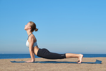 Fototapeta na wymiar Young slender girl doing yoga on the beach on a sunny morning, plank exercise, healthy lifestyle