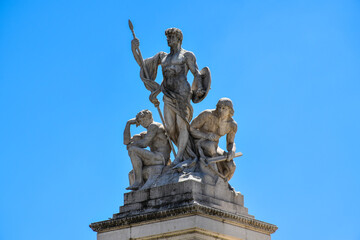 Three statues of people in heroic poses in white marble. Monumental complex of the Vittoriano in Rome.