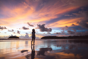 Rear view of young adult tourist asian woman walking relax on beach sand with beautiful dramatic sunset sky