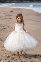 Fototapeta na wymiar Dance on the beach.A beautiful little girl in a white ballet dress walks and dances on a sandy beach