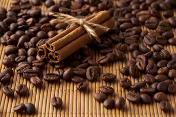 Roasted whole coffee beans and tied sticks of cinnamon on a bamboo mat