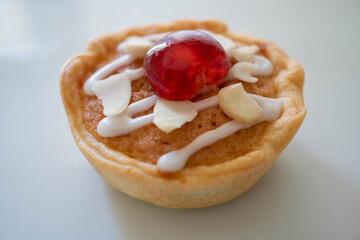 Macro shot of a home baked cherry bakwell decorated with white icing a glacier cherry and flaked almonds. Tart sits on a white plate with white background. Food home baking concept image