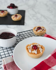 Home baking food concept.  Jam tarts cooling rack and napkins in foreground with cherries and bakewell tarts in background.  Plain backdrop with copy space