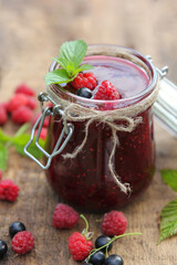 Berry jam in a jar. Preservations. Black currant and raspberry jam, fresh mint, leaves on an old wooden table. Rustic. Background image, copy space, vertical