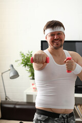 Young attractive man engaged in fitness at home holding dumbbell in hand trying to fight excess weight and loss