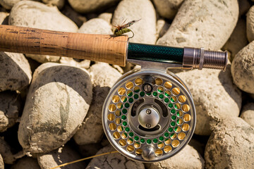 A close up of a trout fly rod, reel and line on rocks, with a cicada fly