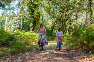 Obraz premium cute little girl and her mom riding a bicycle in a cork oak forest