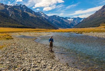 Fototapeta na wymiar An Angler fly fishing for trout on the Ahuriri river, surrounded by mountains, New Zealand