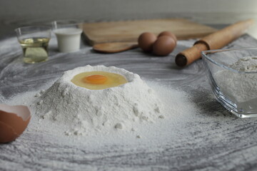 Broken chicken egg in a pile of flour, olive oil, milk, kitchen tool, gray table
