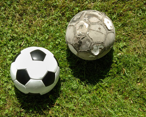 A new and an old football on a green lawn.