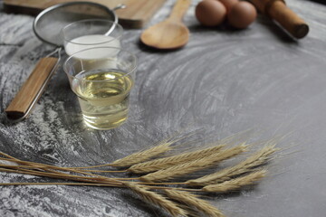 Egg, flour, olive oil, milk, wheat ears, kitchen tool on gray table background.
