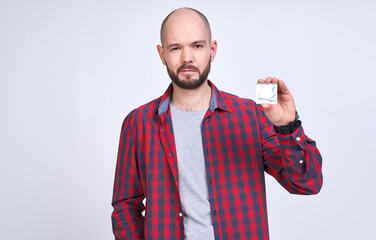 A young man in a plaid shirt holds a contraception in his hand.