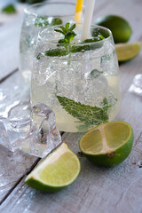 two refreshing cocktails with green ingredients in glass jugs standing on white wooden background