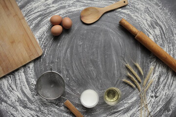 Fototapeta na wymiar Egg, flour, olive oil, milk, wheat ears, kitchen tool on gray table background.