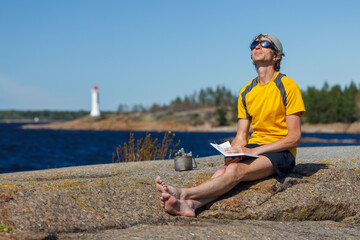 Man with a book and a mug of tea outdoors. Sea background blurred.