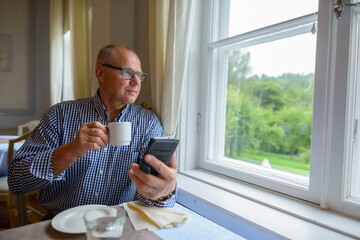 Portrait of senior businessman drinking coffee and using phone at home