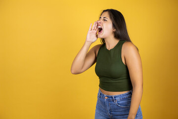 Young beautiful woman standing over yellow isolated screaming with her hand in her mouth