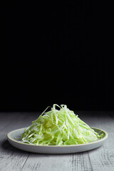 Chopped cabbage salad in plate on wooden background over black backdrop with copyspace.