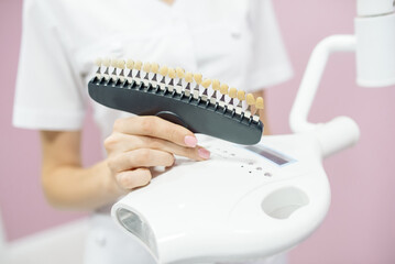 The nurse holds samples of the color of the enamel of the teeth for demonstration to the patient during the procedure of hardware teeth whitening in the cosmetology center