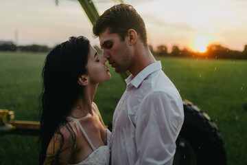 Couple in love embraces on lawn under water drops at sunset.