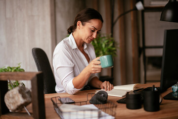 Young businesswoman drinking coffee in her office. Beautiful businesswoman enjoying in the mornings