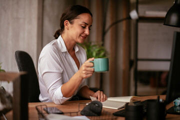 Young businesswoman drinking coffee in her office. Beautiful businesswoman enjoying in the mornings