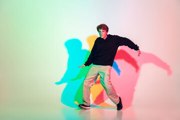 Fototapeta na wymiar Young beautiful man dancing hip-hop, street style isolated on studio background in colorful neon light. Fashion and motion, youth, music, action concept. Trendy clothes. Copyspace for ad.