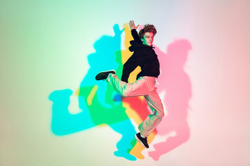 Young beautiful man dancing hip-hop, street style isolated on studio background in colorful neon light. Fashion and motion, youth, music, action concept. Trendy clothes. Copyspace for ad.