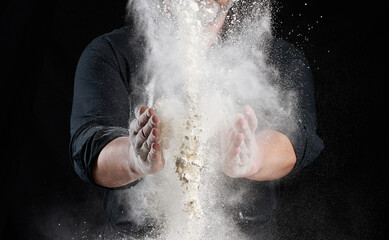 chef in black uniform sprinkles white wheat flour in different directions, product scatters dust