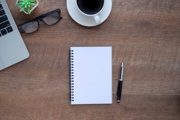 Top view above of Notebook on wooden office desk table with laptop and coffee cup with equipment other office supplies.