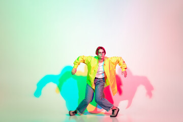 Young beautiful woman dancing hip-hop, street style isolated on studio background in colorful neon light. Fashion and motion, youth, music, action concept. Trendy clothes. Copyspace for ad.
