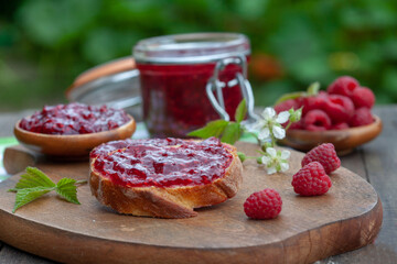 Raspberry jam with fresh raspberries and bread slices on a wooden table. Homemade marmalade, perfect for light, sweet breakfast.