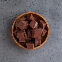 Milk chocolate slices in a wooden plate on a gray background. Raw chocolate, healthy sweets. Food photo.