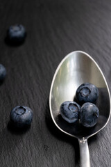 Several blueberries on a metal spoon. Black stone background. Great background.