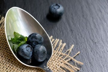 Several blueberries on a metal spoon. Black stone background. Great background.