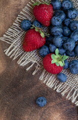 Set of summer berries on burlap napkin and wooden background. Blueberries, raspberries, and...