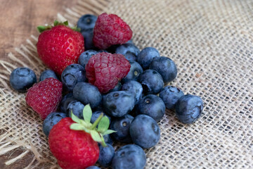 Set of summer berries on burlap napkin and wooden background. Blueberries, raspberries, and strawberries are a varied healthy snack. Yummy.