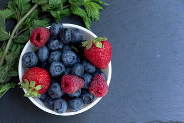 Set of summer berries in a small white bowl on a blackboard. Blueberries, raspberries, and strawberries are a varied healthy snack. Yummy.