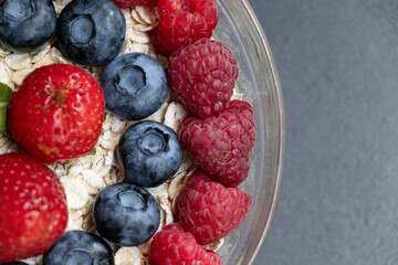 Set of summer berries with oatmeal and chia seeds in a small glass bowl on a black stone background. Perfectly healthy summer breakfast. Yummy.