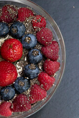Set of summer berries with oatmeal and chia seeds in a small glass bowl on a black stone background. Perfectly healthy summer breakfast. Yummy.