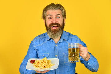 beer and french fries in restaurant. eating and drinking at bar. hipster relax in tavern. bearded guy having snack. lazy man enjoying fresh beer and junk food. man with fast food