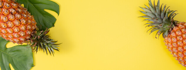 Fototapeta premium Beautiful pineapple on tropical palm monstera leaves isolated on bright pastel yellow background, top view, flat lay, overhead above summer fruit.