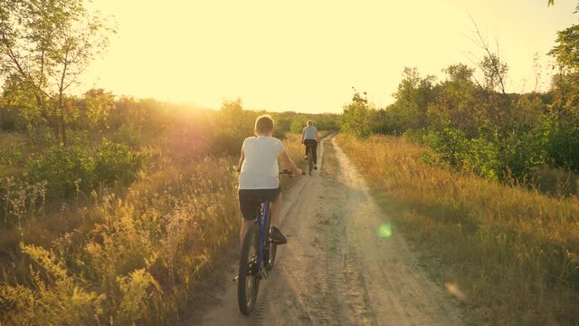 Happy family, mother and son in the park ride a bicycle along the path in the forest in the rays of beautiful sunset. A family of cyclists. Athletic family. A healthy lifestyle.