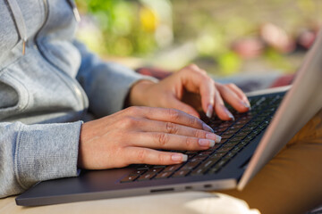 Fototapeta premium Woman uses a notebook computer outdoors close-up. The background is blurred.