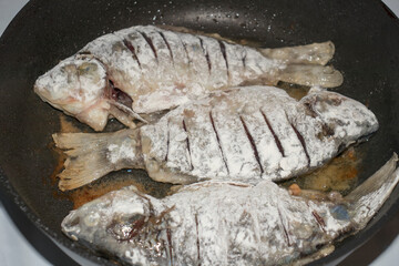 Three carp fish are fried in a pan