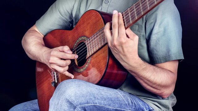 Classical guitarist plays piece of music. Men musician plays classical guitar. Beautifull woodem acoustic instrument close up.