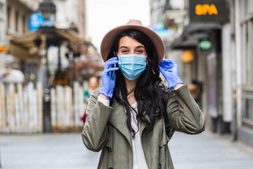 Fototapeta premium Young woman on the street wearing face protective mask to prevent Coronavirus COVID-19 and anti-smog and using smartphone