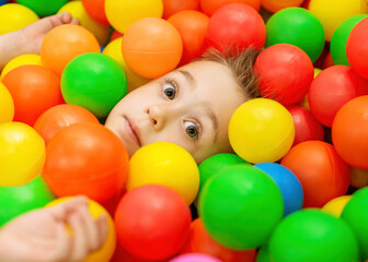 Fototapeta na wymiar Portrait of funny child in playroom. Caucasian boy in a pool with colorful balls