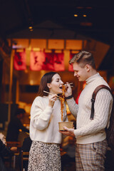 newlywed couple eating noodles with chopsticks in Shanghai outside a food market near Yuyuan. Couple eating authentic local food. husband and wife eating chinese food outisde of a food hall
