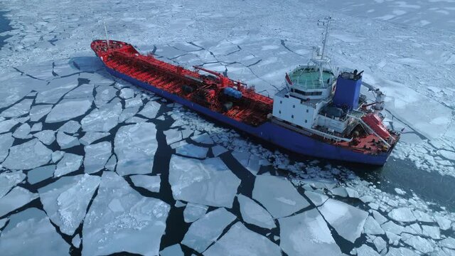 Aerial above epic huge steel icebreaker breaks ice by bow of ship and floats in large sea ice floes. Maintaining navigation in a frozen sea channel laying. Self-propelled specialized vessel red ship
